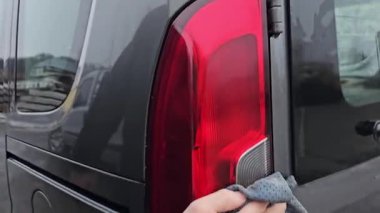Adamın biri gri bir arabanın arka lambasını paçavrayla siliyor. Yüksek kalite 4k görüntü