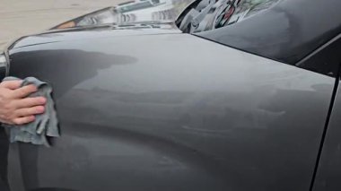 Yakın plan. Bir adam gri bir arabanın yüzeyini parlayana kadar bezle siler, arabayı yıkar, yıkadıktan sonra nemi temizler. Yüksek kalite 4k görüntü