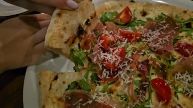 Büyük, taze pişmiş bir pizza, dilim dilim doğranmış. Sahne pizzanın karşı konulmaz çekiciliğini vurguluyor. İnsanlar lezzetli yemeğin kendilerine düşen kısmının tadını çıkarıyorlar. Yüksek kalite 4k görüntü