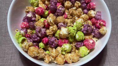 Renkli patlamış mısır, daire şeklinde dönüyor. Tatlı patlamış mısırın yakın çekimi, üst manzara. mor yeşil karamel kırmızı patlamış mısır beyaz bir tabağa döküldü.