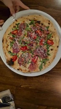 Eritilmiş mozzarella peynirli taze İtalyan pizzası, domuz pastırması jambonu ve roka yaprakları beyaz masadaki tabakta. Yüksek kalite 4k görüntü