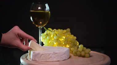 Peynirli peynirli kız mutfakta gül şarabıyla cam tutuyor. Zarif kremalı camembert yemeği ve alkollü üzüm suyu. peynirli şarap üzümleri koyu arka planda... peynir tadı veren lüks yiyecekler...