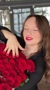 Siyah ceketli, Avrupalı, kırmızı dudaklı, büyük bir buket kırmızı çiçekle 51 gül taşıyan genç, güzel bir kız 8 Mart 'ta yeni yıl tatili için bir restoranda evlenme teklif ediyor. Yüksek