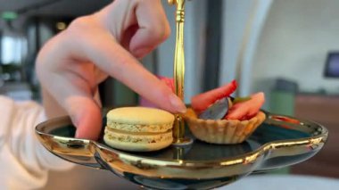 Bir el, yanında ferahlatıcı bir içecek ile tamamlanmış, peçetenin üzerinde dinlenen canlı bir makarona uzanır. Atmosfer rahat ve davetkar, tatlı bir ikram için mükemmel. 4k görüntü
