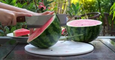 Asyalı kadın elini, tahta kesme tahtasındaki taze karpuz dilimleri ve parçaları kesmek için bıçak kullanarak kapat. Yüksek kalite 4k görüntü