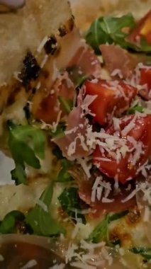 Büyük, taze pişmiş bir pizza, dilim dilim doğranmış. Sahne pizzanın karşı konulmaz çekiciliğini vurguluyor. İnsanlar lezzetli yemeğin kendilerine düşen kısmının tadını çıkarıyorlar. Yüksek kalite 4k görüntü