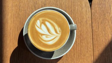 Bir fincan kapuçinoyu kapuçinoya kapat. Kahve köpüğüne çizilmiş bir kalbin üst görüntüsü. Sabah kahvesi ahşap kahverengi bir masanın üzerinde duruyor. Kopyacı. Bir fincan kahve çiçeği ahşap masaya çiziyor.