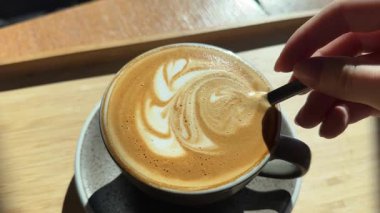 Stajyer bayan kahveci Kakao karıştırma alıştırması için hazırlanıyor. Kahvenin yüzeyine latte resmi çizmek için. Çiçek desenli güzel bir örnek. Bir fincan kahve çiçeğinin ahşap masaya çizimi.