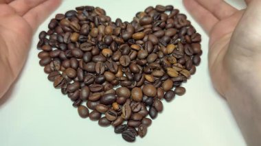 Kalp şeklinde kahve çekirdeği tutan kadın elleri dikkatli, keyifli ve tutkulu kahve. Kahve ve kafein aşkı kavramı. Arkaplanda tahıllar ve çuval bezi var. kahve çekirdekli kalp