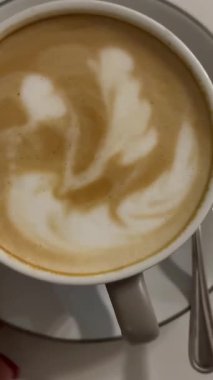 Bir fincan kahve cappuccino ve kahve tablosu, en iyi manzara. Latte sanat kahvesi masada içilmeye hazır. Sabah kahvesi aromalı kapuçino. Yüksek kalite 4k görüntü