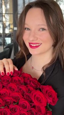 Siyah ceketli, Avrupalı, kırmızı dudaklı, büyük bir buket kırmızı çiçekle 51 gül taşıyan genç, güzel bir kız 8 Mart 'ta yeni yıl tatili için bir restoranda evlenme teklif ediyor. Yüksek