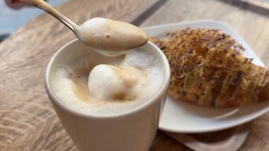Fransız kruvasanı ve bir fincan kahve. Kahve fincanına şeker koymak ve karıştırmak. Dubai çikolatalı kruvasan, kahve kruvasan köpüğü.