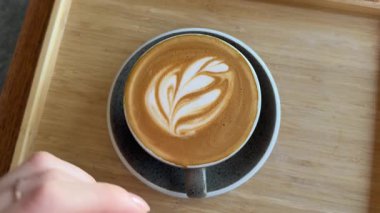 Kadınların elleri bir fincan kahve alır ve masanın üzerine kaldırır, köpüğe Rosetta resmi çizilir. Süt köpüğünden yapılan ince ve kısa ömürlü bir sanat olan lezzetli bir içecek. Yüksek kalite 4k görüntü