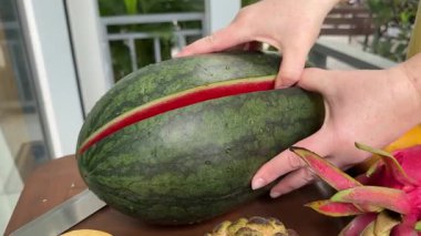 Kadın elleri kesme tahtasında olgun karpuz kesiyor. Ellerinle karpuzu ikiye böl.