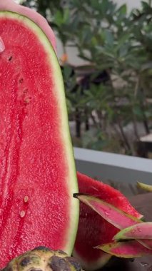 Canlı etini dilimlerken, sulu, kırmızı bir karpuzu sıkıca tutan bir elin yakın çekimi, taze, yeşil kabuk, meyveyi tek tek keserken pembe iç kısmıyla çelişiyor. Yüksek kalite 4k görüntü