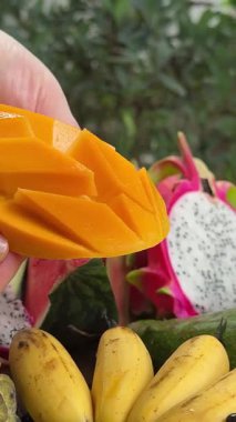 Taze mango ve dilimlenmiş parçaları ahşap bir masada, canlı tropikal meyveler sergiliyor. Mutfak ve sağlıklı yaşam tarzları için mükemmel. Yüksek kalite 4k görüntü