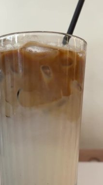 Kahve dükkanında elinde pipetle buzlu latte kahve içen bir kadın. Soğuk yaz içeceği. Yüksek kalite 4k görüntü