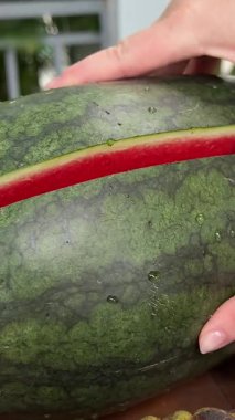 Kadın elleri kesme tahtasında olgun karpuz kesiyor. Ellerinle karpuzu ikiye böl.