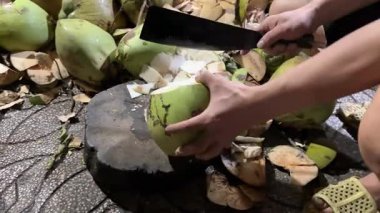 Bir adamın hindistan cevizini büyük bir bıçakla, açık mutfakta, açık hava ızgarasının yanında keserken orta pozu. Yüksek kalite 4k görüntü