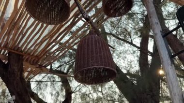 Örülmüş tasarımı ve sıcak parıltısıyla eşsiz tavan lambası görünür ahşap kirişler ve bulanık ön plan çiçekleri ile desenli bir tavana kurulmuş. Yüksek kalite 4k 