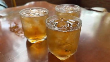 Çay seremonisi. Buzlu çay şeffaf bir bardağa dökülür. Buz küpleri, limon dilimleri ve parlak arka planda duran nane şekeri ile. Modern soğuk Çin töreni. Üç buzlu içecek, yeşil buzlu çay.