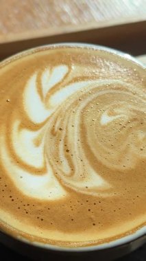 Stajyer bayan kahveci Kakao karıştırma alıştırması için hazırlanıyor. Kahvenin yüzeyine latte resmi çizmek için. Çiçek desenli güzel bir örnek. Bir fincan kahve çiçeğinin ahşap masaya çizimi.