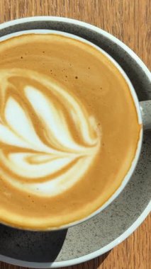 Bir fincan kapuçinoyu kapuçinoya kapat. Kahve köpüğüne çizilmiş bir kalbin üst görüntüsü. Sabah kahvesi ahşap kahverengi bir masanın üzerinde duruyor. Kopyacı. Bir fincan kahve çiçeği ahşap masaya çiziyor.