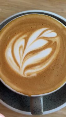 Kadınların elleri bir fincan kahve alır ve masanın üzerine kaldırır, köpüğe Rosetta resmi çizilir. Süt köpüğünden yapılan ince ve kısa ömürlü bir sanat olan lezzetli bir içecek. Yüksek kalite 4k görüntü