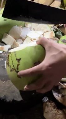 Bir adamın hindistan cevizini büyük bir bıçakla, açık mutfakta, açık hava ızgarasının yanında keserken orta pozu. Yüksek kalite 4k görüntü
