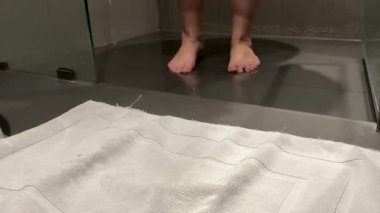 Kadınların bacakları beyaz havluyu açar ve üzerinde dururlar. Duştan sonra, kişisel bakım, banyo, gri arka plan, bir otelde. Yüksek kalite 4k görüntü