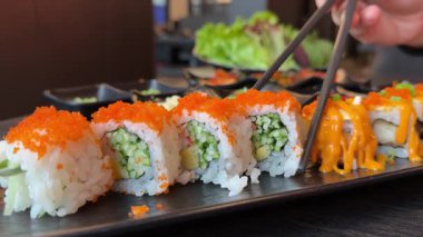 Asya suşisi California 'yı salatalıkla, yemek çubuklarıyla ve sos restoranındaki yemek balıklarına batırır. Yüksek kalite 4k görüntü