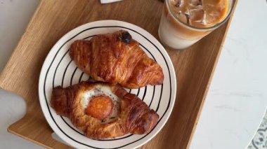 Lezzetli kokulu kahvaltı buzlu kahve ve içinde yumurta olan kruvasan kahveci restoranının kahveli pastalı kahvesinde beyaz bir masada. Yüksek kalite 4k görüntü