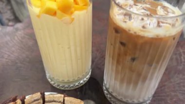 Kafedeki masada iki bardak mango smoothie ve buzlu mağara ve muz lifiyle şerbetli kahvenin kahvaltısı tropikal hava şekerlemeleri. Yüksek kalite 4k görüntü