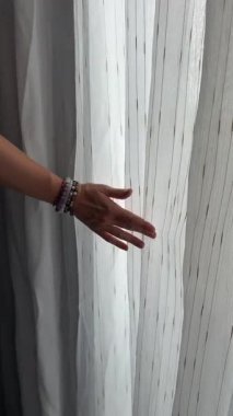 Kız pencerenin önünde duruyor ve elini perdenin üzerinden geçiriyor. O nazikçe perdeye dokunur. Yüksek kalite 4k görüntü