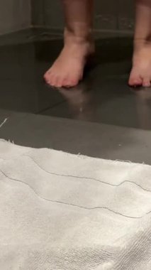 Kadınların bacakları beyaz havluyu açar ve üzerinde dururlar. Duştan sonra, kişisel bakım, banyo, gri arka plan, bir otelde. Yüksek kalite 4k görüntü