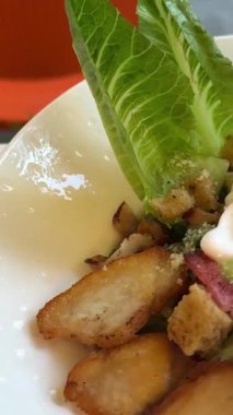 Baştan çıkarıcı Sezar salatası, mavi bir tabakta güzelce düzenlenmiş, ahşap restoran masasında ortaya çıkıyor. Taze marul, ızgara tavuk, vişneli domates, parmesan peyniri...