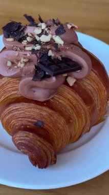 Dekorlu güzel çikolatalı kruvasan, beyaz bir tabağın üzerinde, kafeterya restoranındaki tatlı pastaları sütlü çikolatanın üzerinde duruyor. Yüksek kalite 4k görüntü