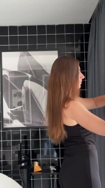 Banyo perdelerini indiren genç bir kadın büyük pencerenin keyfini çıkarıyor. Yeni güne taze düşüncelerle başlayan bir kız. Yeni başlangıçlar, siyah elbiseli kadın lüks villada perdeleri açıyor.