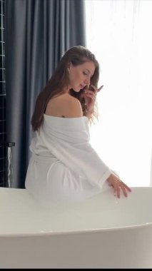 Kadın suya banyo tuzu koyuyor. Yakın plan. Meçhul bir kadın mumların önünde köpük küveti hazırlıyor. İsimsiz beyaz elbise modelinin dinlenme gecesi atmosferi rutin cilt bakımına sahip.