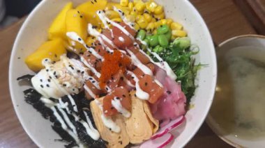 Yüksek açılı çekim, suşi alma seçenekleriyle dolu iki kağıt kaseyi gözler önüne seriyor. Kızarmış suşi sosislileri ve tobiko ile karides dürümleri de dahil. Kırsal ahşap bir bankta.. 