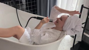 Komik kadın köpükle dolu bir küvette oturur, duşta şarkı söyler. Banyoda baştan aşağı köpüklü bir kadın oynaşıyor. Bir kız duşta şarkı söylüyor.