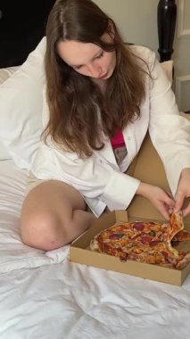 Pizza yiyen küçük bir kız. Aç, mutlu, genç bir kadın bir dilim pizza yiyor. Evde, pizzacıda pizza yiyor. Fast food, çocuklar, sağlıksız yemek konsepti.. 