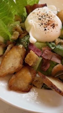 Baştan çıkarıcı Sezar salatası, mavi bir tabakta güzelce düzenlenmiş, ahşap restoran masasında ortaya çıkıyor. Taze marul, ızgara tavuk, vişneli domates, parmesan peyniri...