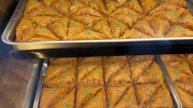 Kırsal tepside dinlenen altın katmanlı baklava geleneksel pastaların karmaşık katmanlarını ve profesyonel fırın ortamında parlayan şurubu sergiliyor. Yüksek kalite 4k görüntü