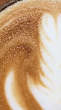 Mavi seramik bardakta güzel latte sanatıyla kapuçino ve güzel bir latte sanatı. Öğle yemeğinde leziz kahvenin dikey videosu. Yüksek kalite 4k görüntü