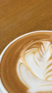 Bir fincan kahve çiçeğinin ahşap masa üzerine çizimi stajyer kadın kahveci barista karıştırma kakaosu kahvesinin yüzeyine latte sanatı çizme alıştırması için hazırlan, güzel çiçek desenli örnek. Yüksek kalite 4k