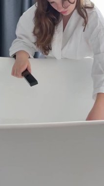 Kız küveti suyla dolduruyor köpük banyosu için sabun hazırlıyor beyaz bornozlu genç kadın. Yüksek kalite 4k görüntü