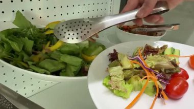 Fresh salad with lettuce leaves and tomato falling into bowl, served with healthy food ingredients on white table, slow motion. High quality 4k footage