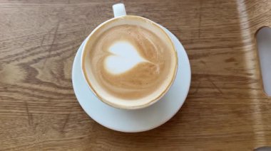 Latte lezzetli aromatik kahve kapuçino masanın üzerinde duruyor ve kamera da fincan sanatının kalbinin etrafında dönüyor. Yüksek kalite 4k görüntü