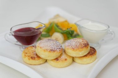 İçinde toz şekerle toz haline getirilmiş üç pofuduk peynirli krep bulunan bir tabak, üzerine beyaz bir tabakta zarif bir şekilde düzenlenmiş kremalı ricotta sosu ile birlikte. Yüksek kalite fotoğraf